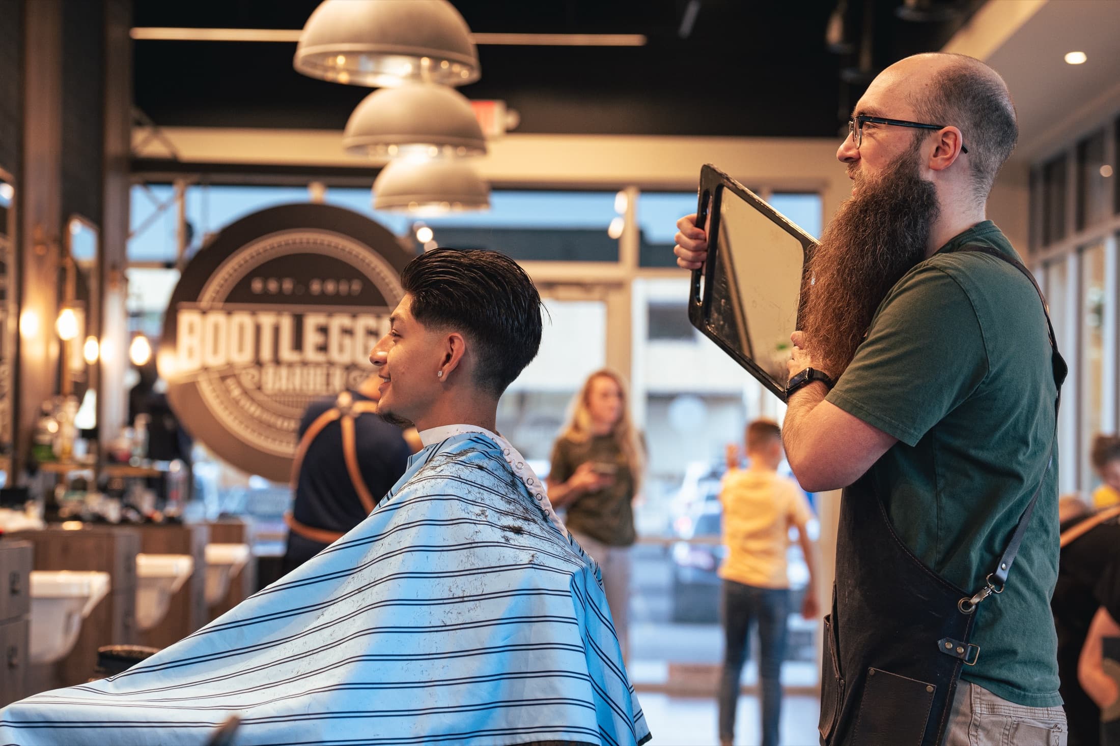 Client in a striped cape admiring his fresh pompadour fade in a hand mirror