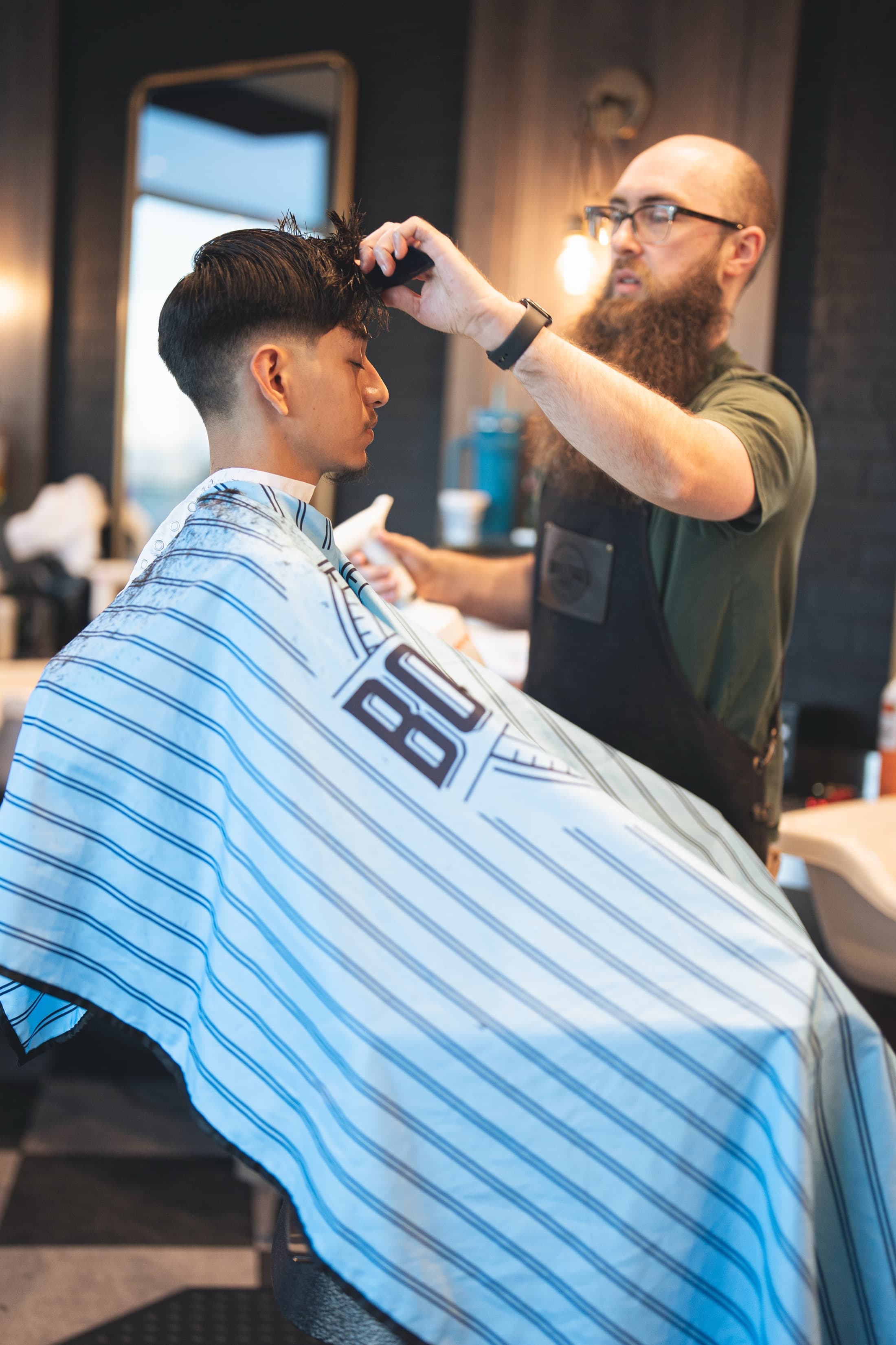 Barber combing and sectioning a client's textured hair in a pinstriped Bootlegged cape