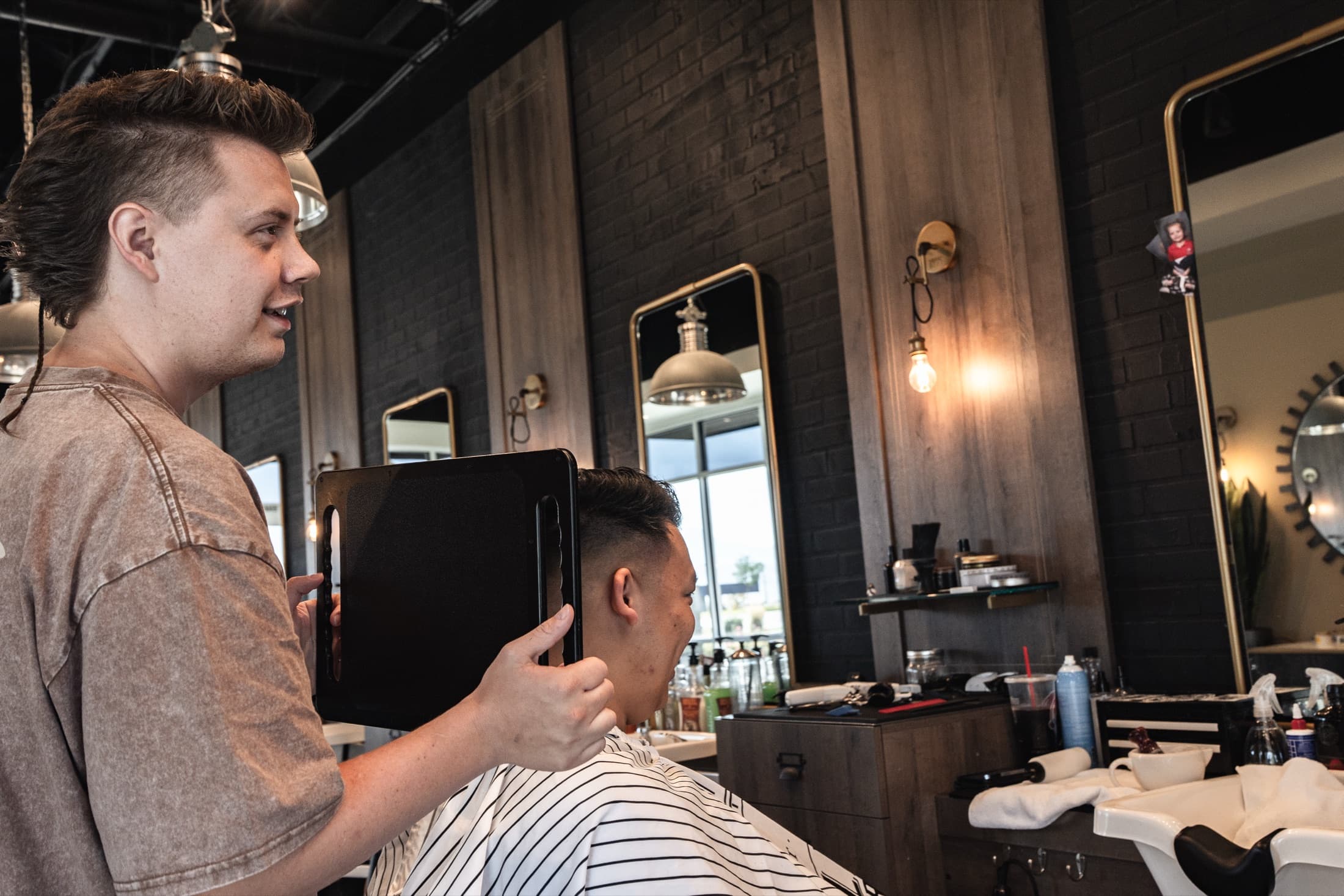 Barber showing a grinning client the finished back of his cut in a hand mirror